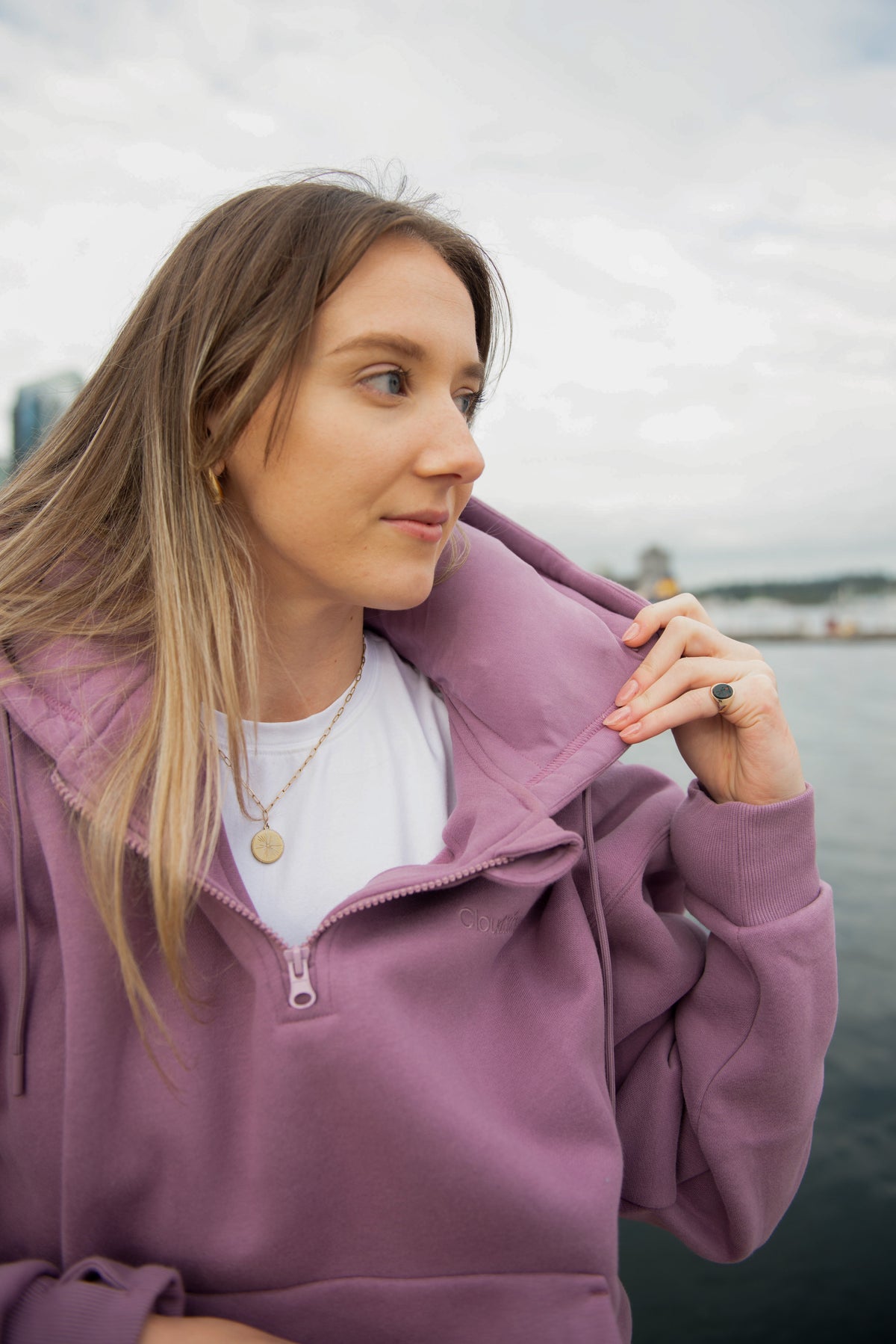 Model adjusting the built-in neck pillow in the purple Travel Hoodie